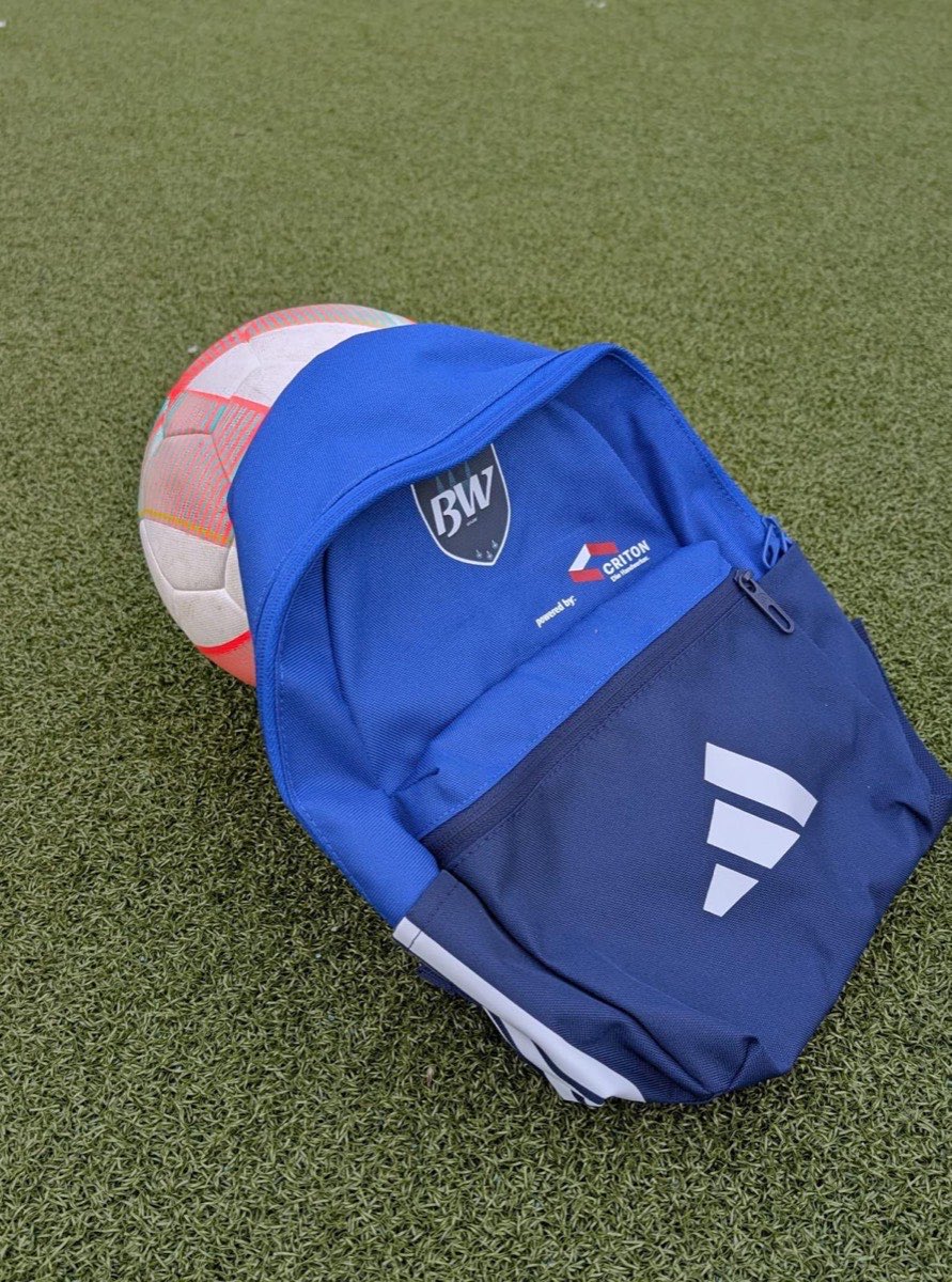 Blauer Sportrucksack mit Vereinswappen und „powered by CRITON“-Logo neben einem Fußball auf dem Rasen