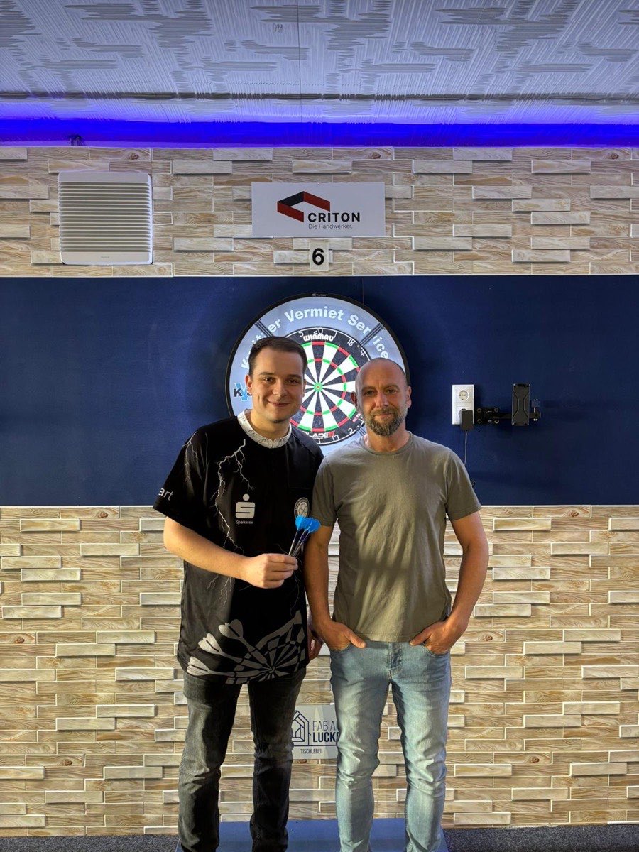 Zwei Dartspieler vor der Dartscheibe unter einem CRITON-Schild im Vereinsraum