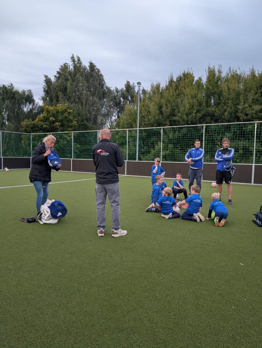 Trainer übergeben den Kindern der Fußballmannschaft auf dem Platz neue blaue Sportrucksäcke